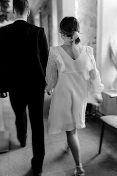 Back view of a couple in stylish attire walking indoors in black and white.