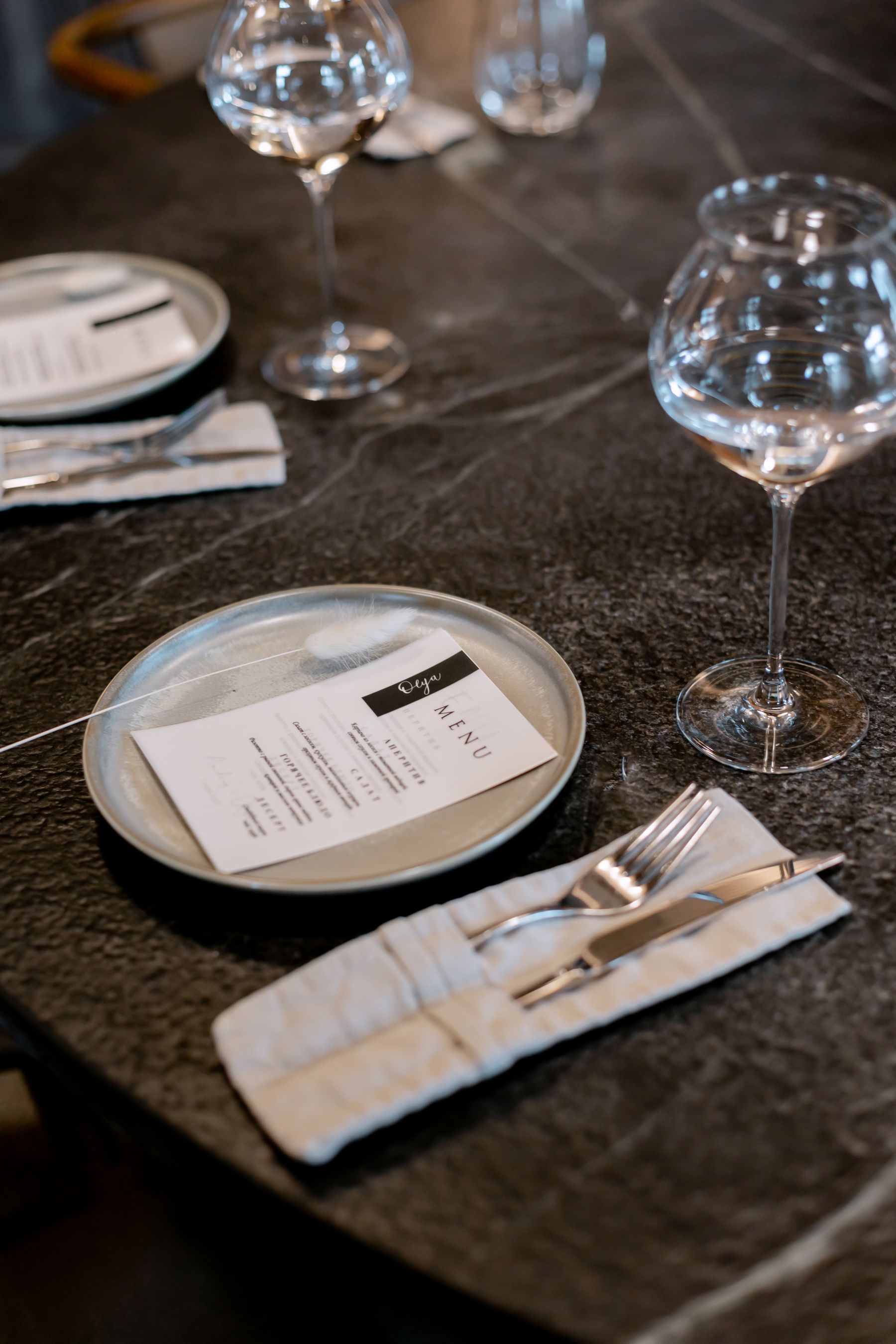 Plates glassware and cutlery arranged on a dark dining table