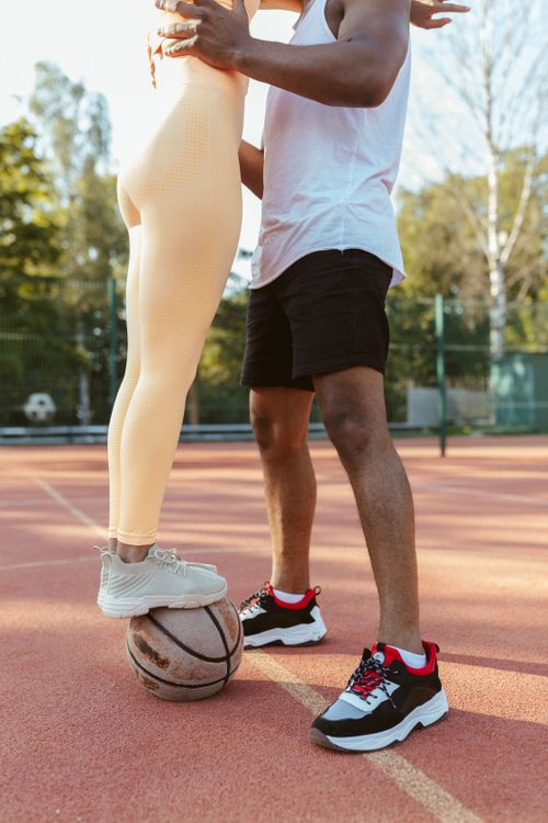 Free Playful couple standing on a basketball court, woman's feet on a basketball. Stock Photo