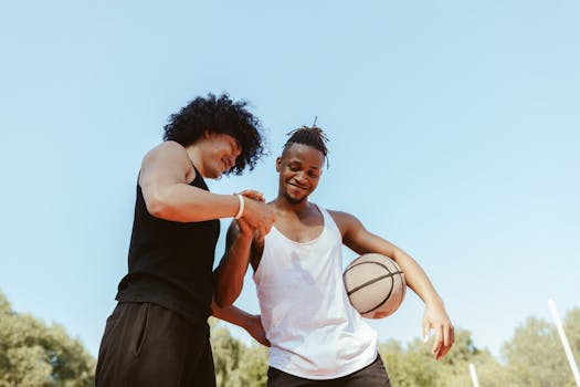 Two friends playing basketball outdoors, enjoying a sunny day.