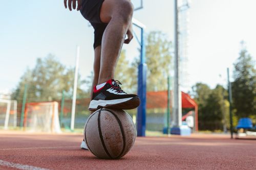 Free A person standing on an outdoor basketball court with a foot on a basketball, showcasing sports footwear. Stock Photo