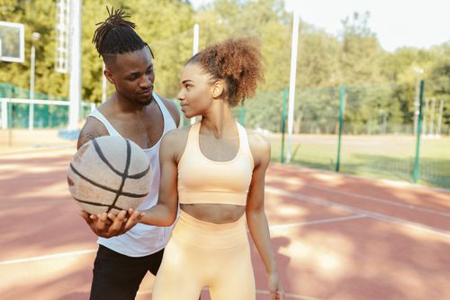 Free A young couple enjoys basketball on a sunny outdoor court, fostering connection and fitness. Stock Photo
