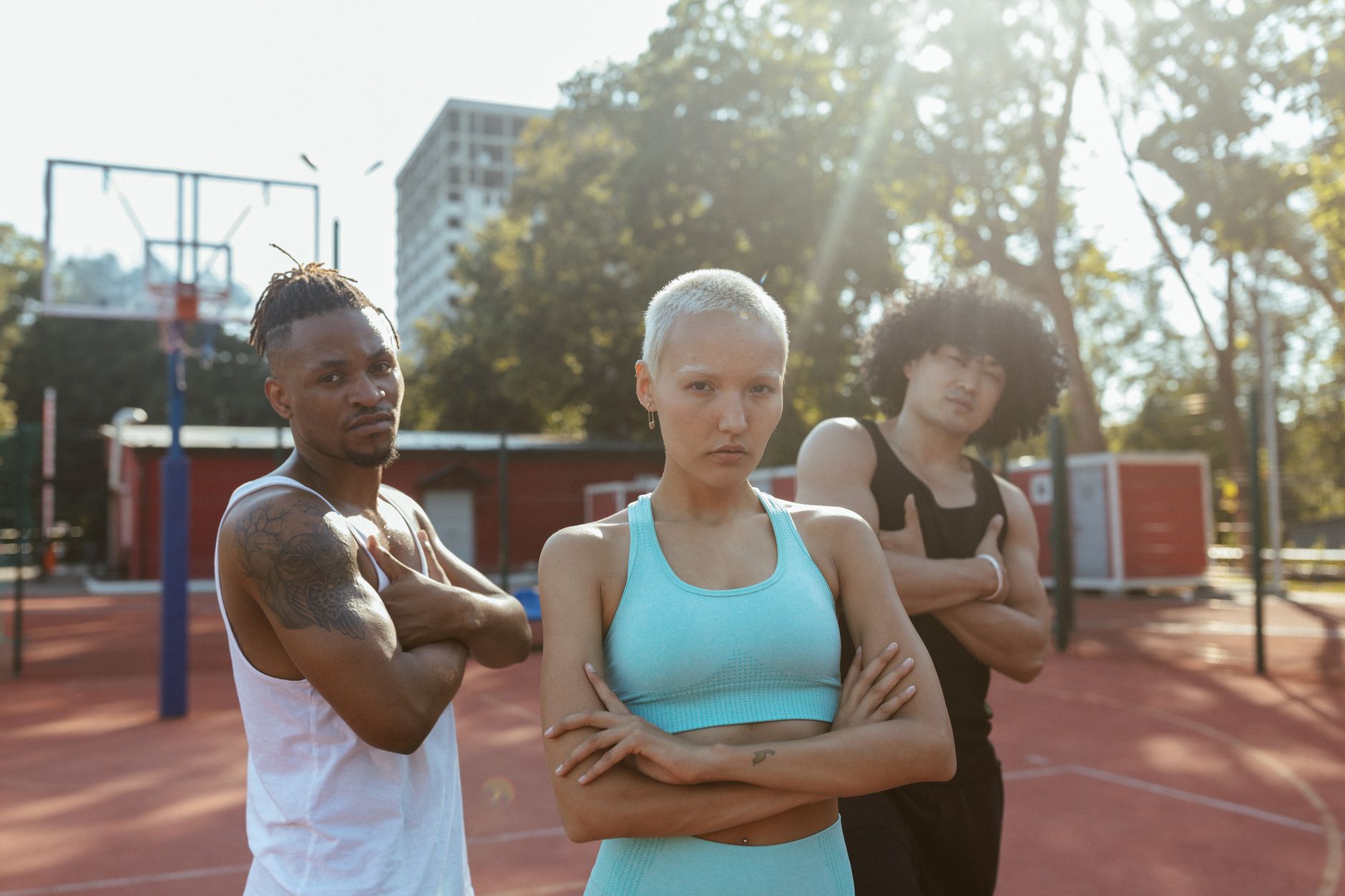 Three individuals in activewear stand confidently on a sunny outdoor basketball court.