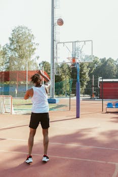 Adult man shooting a basketball into the hoop on an outdoor court under sunny skies.