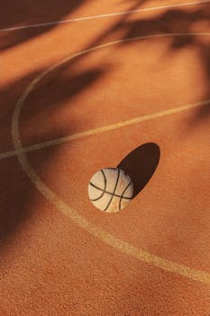 A basketball rests on an outdoor court with distinct shadows and warm lighting.