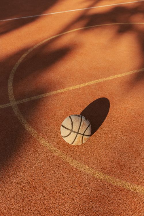 Free A basketball rests on an outdoor court with distinct shadows and warm lighting. Stock Photo