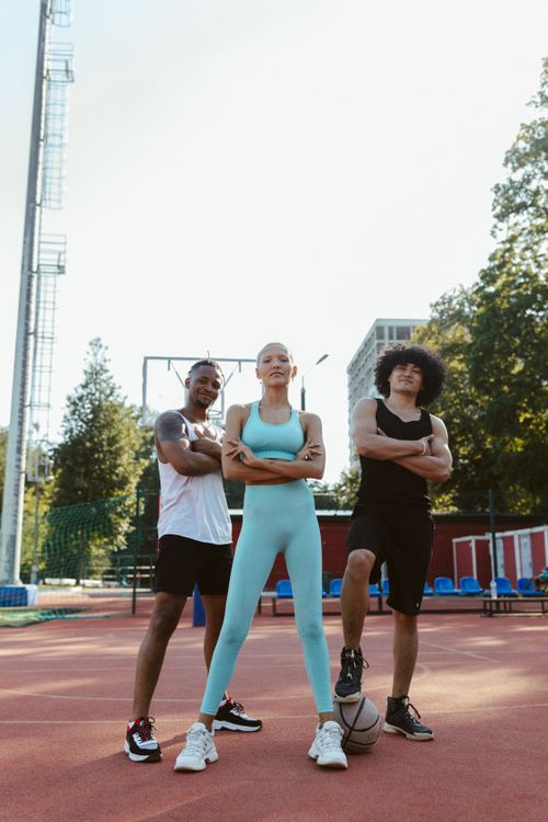 Free Three adults in athletic wear pose confidently on an outdoor basketball court. Stock Photo