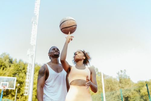 Free A couple in activewear playing basketball outdoors on a sunny day. Stock Photo