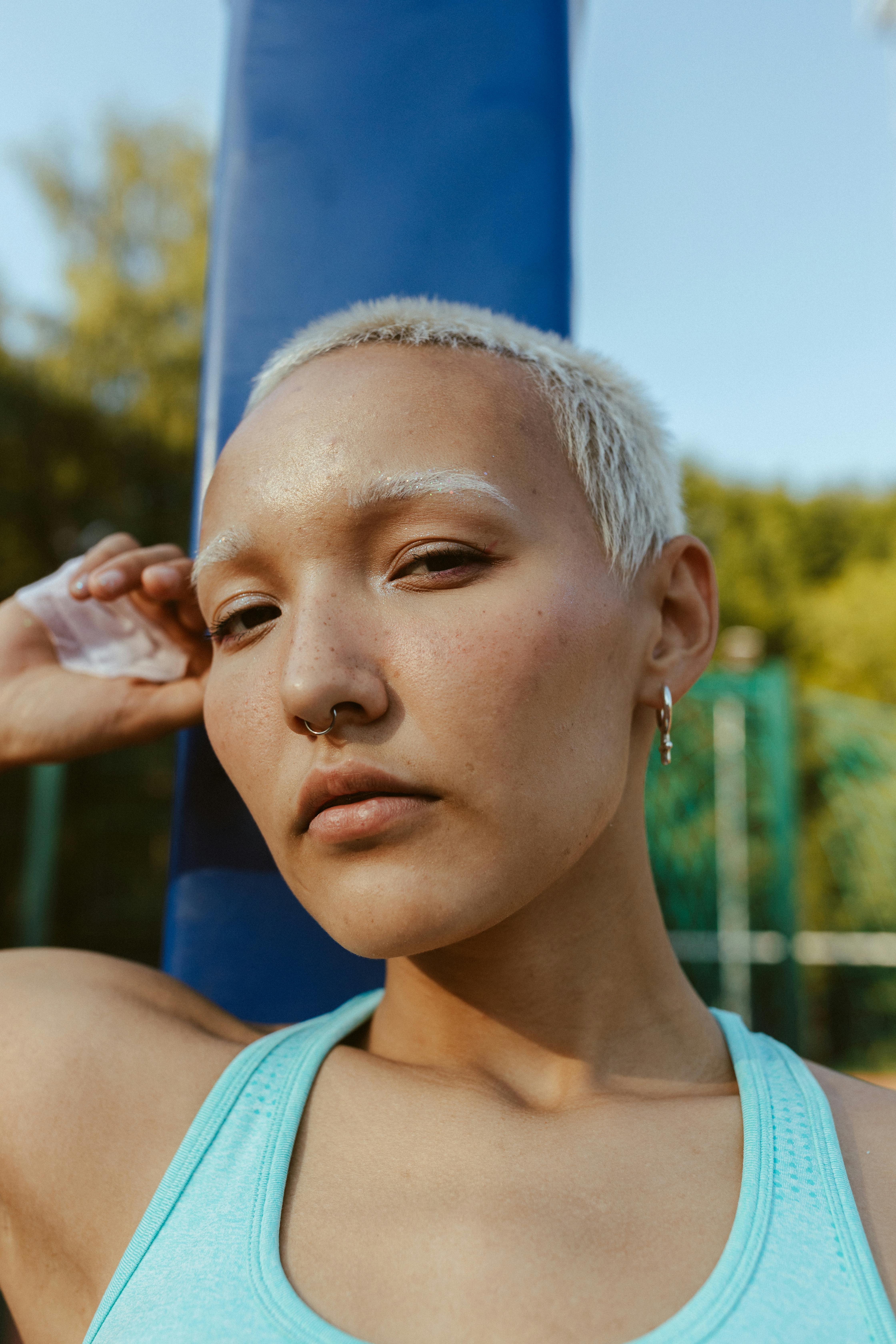 Portrait of a stylish young adult with short hair, earring, and nose piercing outdoors, exuding confidence.