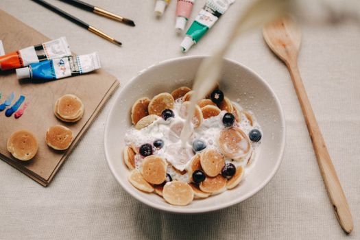 Mini pancakes with blueberries and milk beside art supplies, combining creativity and breakfast.