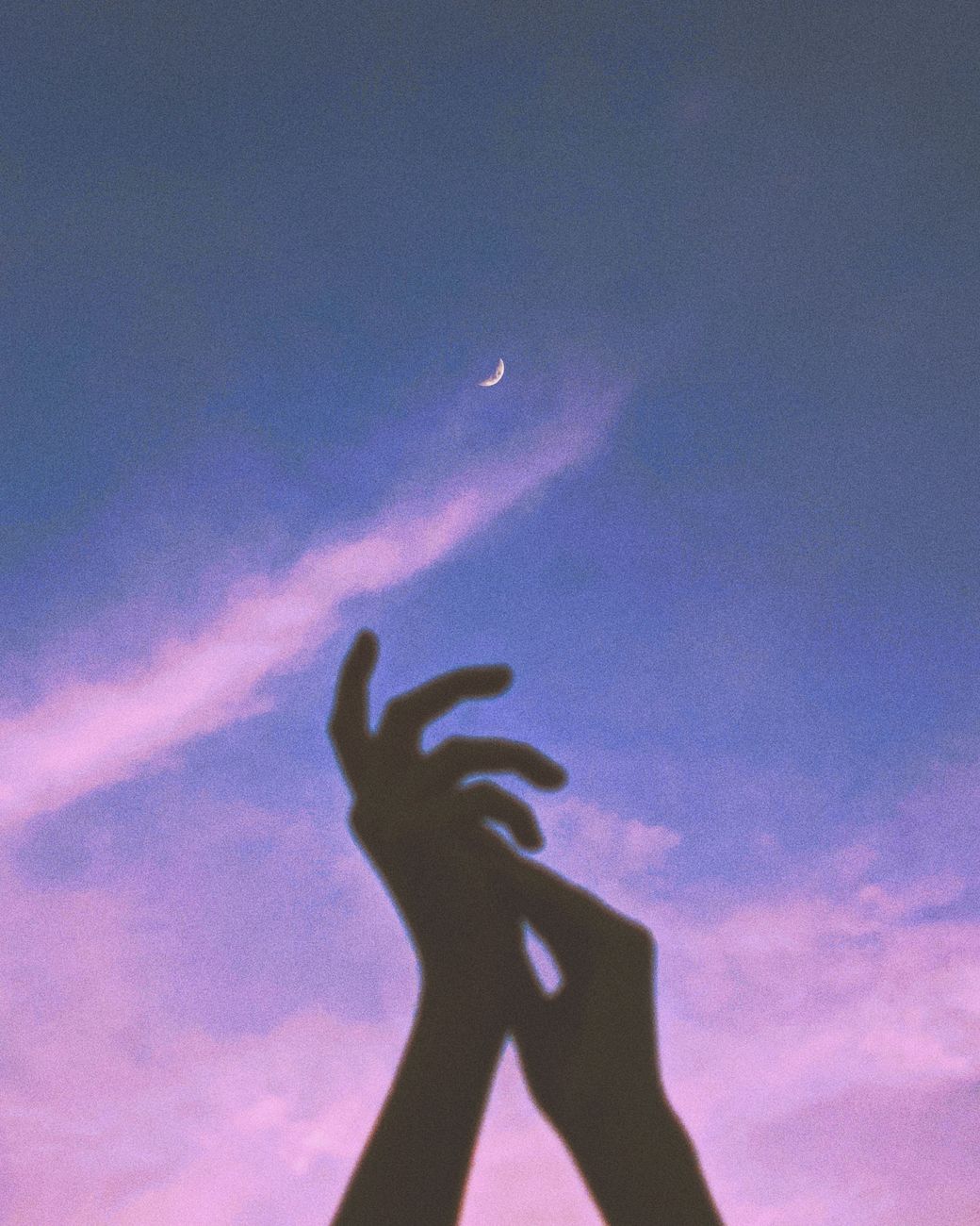 Silhouette of hands reaching towards the crescent moon in a twilight sky.