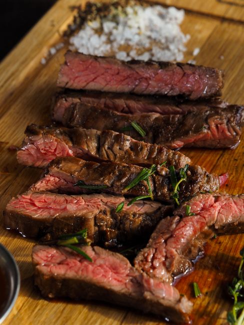 Sliced grilled arrachera steak with charred crust and pink interior, resting on a wooden cutting board next to lime wedges and a small bowl of salsa.