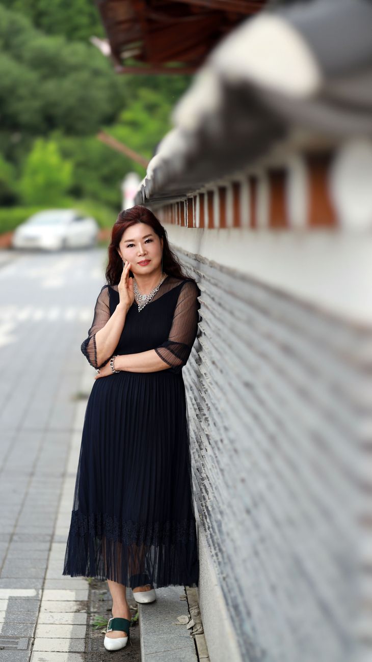 Elegant woman in black dress leaning against a wall on a quiet street.