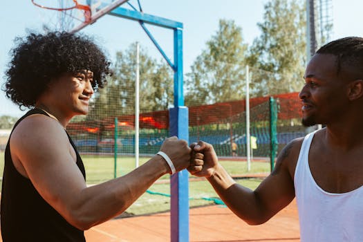 Two young men sharing a fist bump outdoors on a basketball court, symbolizing friendship and teamwork.