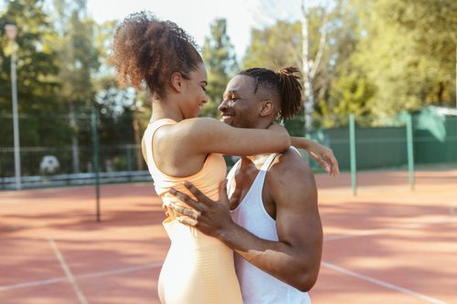 Free Smiling couple embraces on tennis court, enjoying a sunny day outdoors. Stock Photo