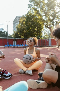 Smiling woman in activewear with friends, holding a basketball at an outdoor court.