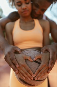 A couple forms a heart shape with hands on a basketball, symbolizing unity and love.