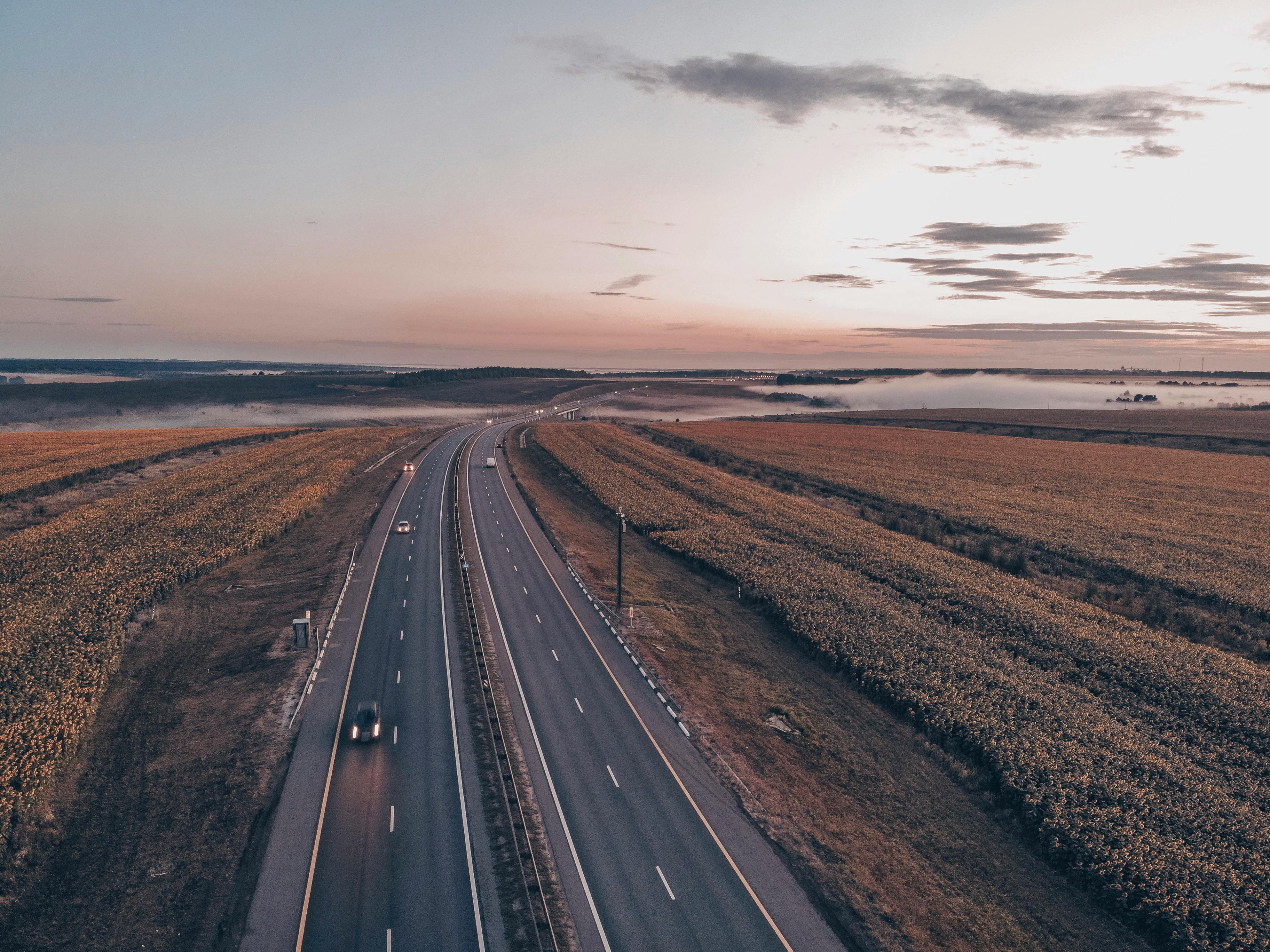 Aerial view of a tranquil rural highway surrounded by fields during sunset, capturing the serene landscape.