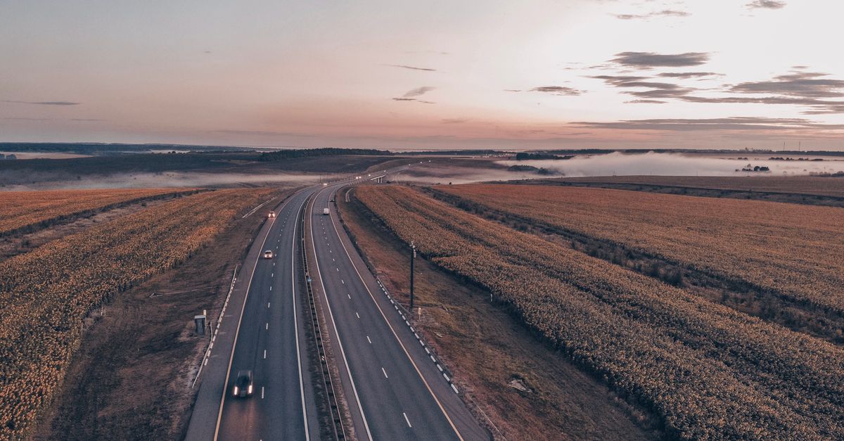 Aerial view of a tranquil rural highway surrounded by fields during sunset, capturing the serene landscape.