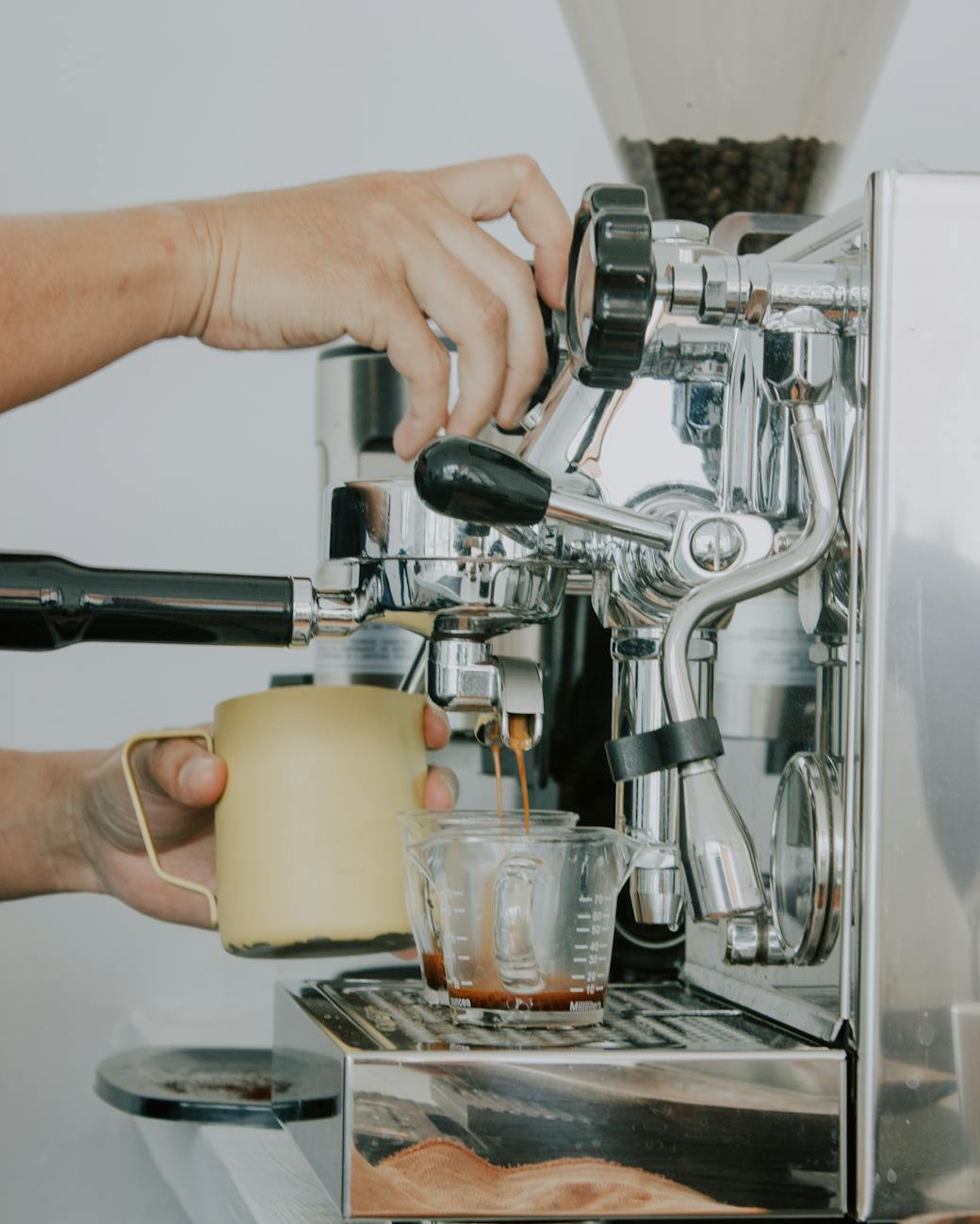close-up of hands operating a coffee machine, pouring espresso into a glass cup.