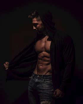 Dark dramatic portrait of a muscular man in a hoodie showcasing abs and fit physique.