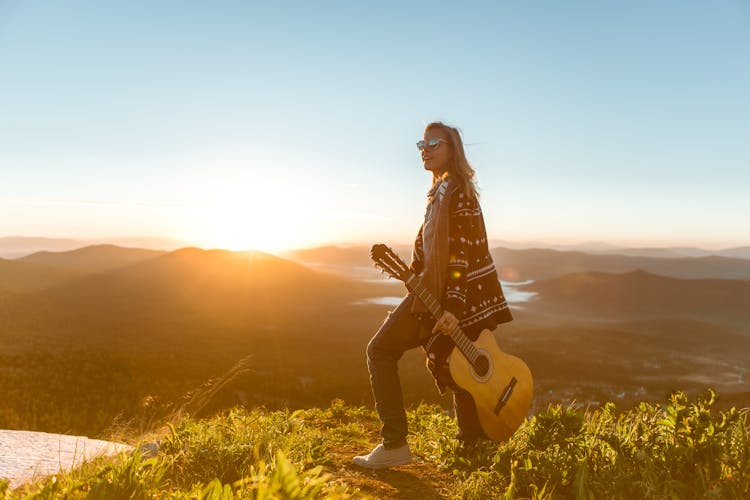 Woman On Top Of Highland Holding A Brown Guitar