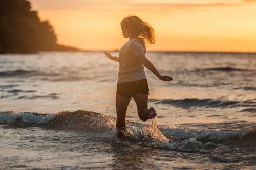 Free A woman splashing in the ocean during a serene sunset, capturing joy and freedom. Stock Photo