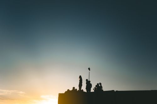 Free A group of people silhouetted against a sunset sky, standing on a rooftop. Stock Photo