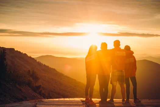 A group embraces at a mountain overlook during a beautiful sunset, creating a warm silhouette.