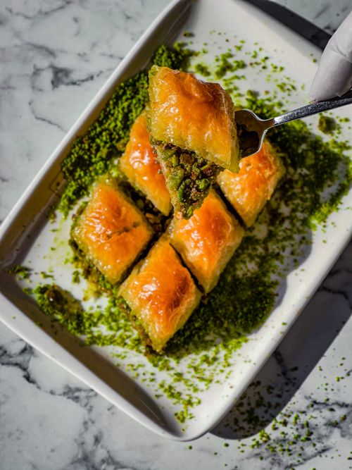 Free Close-up of golden baklava slices with pistachio on a marble background, presented on a white plate. Stock Photo
