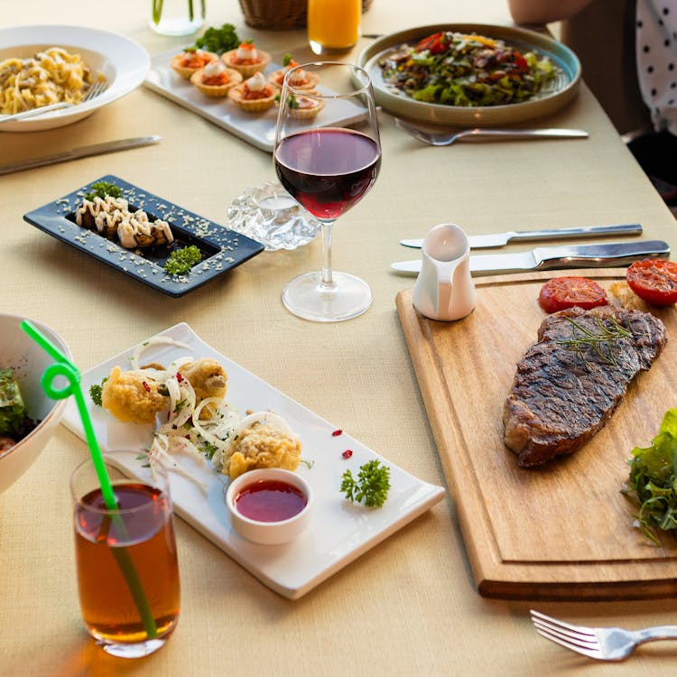 Steak On A Wooden Board And Food Platters On A Table