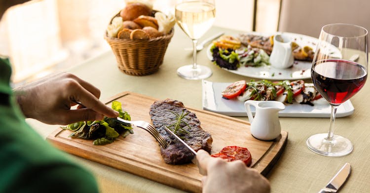 Person Slicing Steak On A Wooden Chopping Board