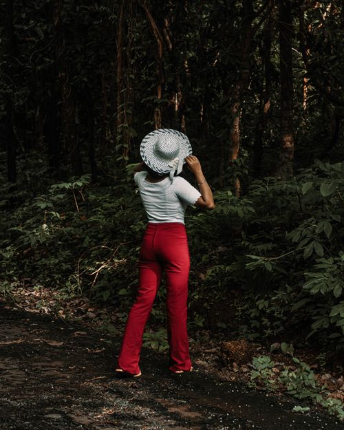 Free A woman wearing red pants and a white hat stands in a lush forested area, embracing nature. Stock Photo