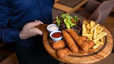 Hand Holding Round Wooden Chopping Board with Food