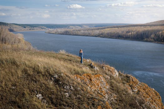 A lone traveler enjoys a scenic view of a river from a cliffside in Russia during fall.