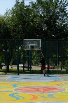 A basketball player shoots a hoop on a colorful outdoor court surrounded by trees.