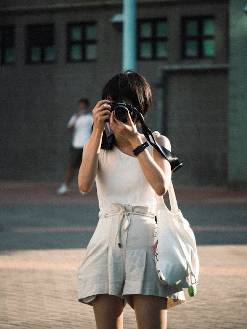 Woman in White Tank Top and Shorts Holding Black Dslr Camera