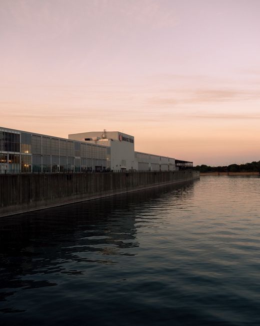 A modern industrial facility along Montreal's waterfront at sunset, reflecting in calm waters.