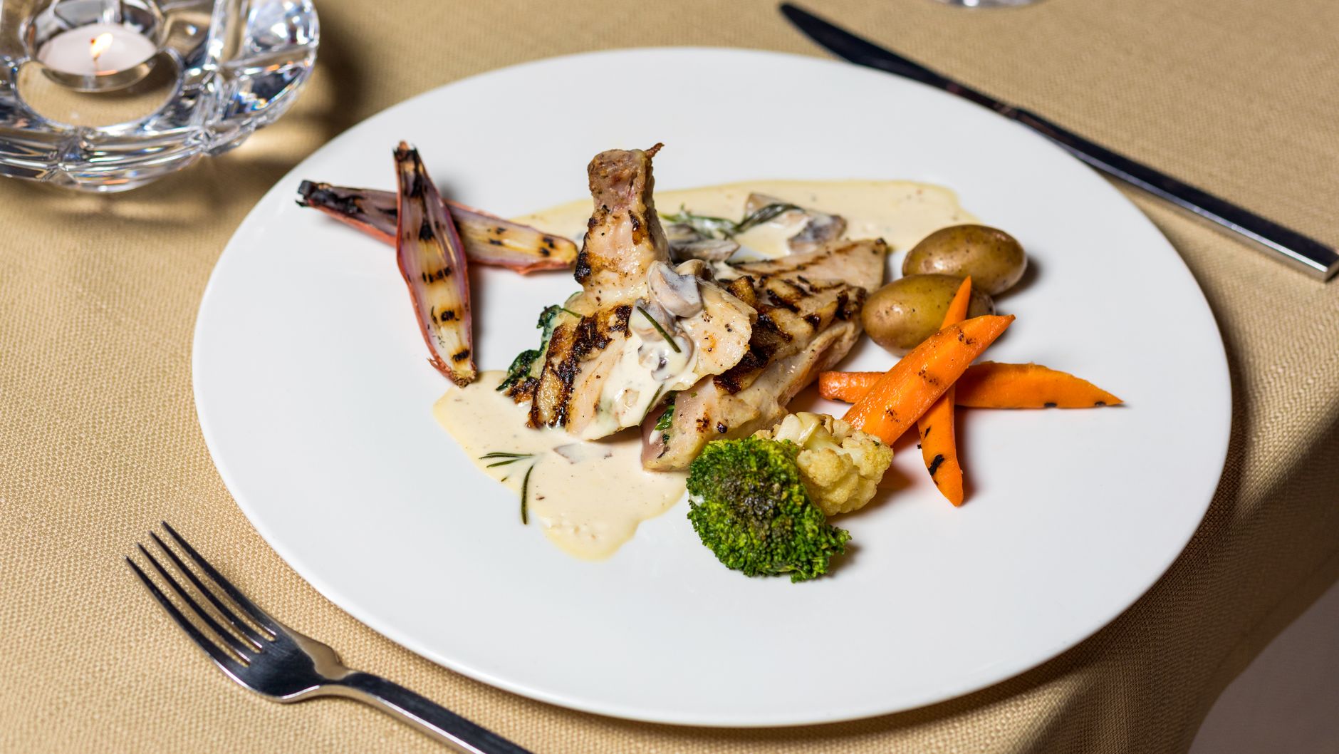 Grilled chicken with creamy sauce, served with vegetables on elegant dining table.