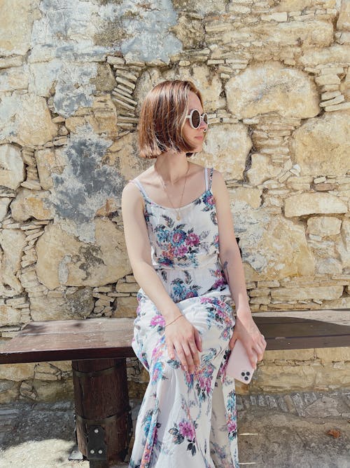 A Woman in Floral Dress and Sunglasses Sitting on a Wooden Bench