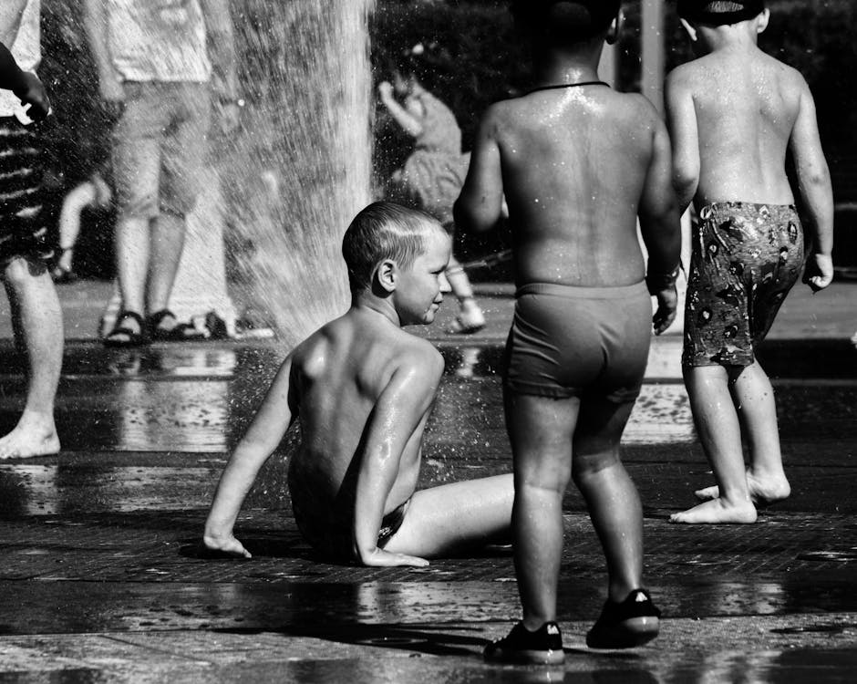 A Grayscale Photo of Children Playing on Water Fountain