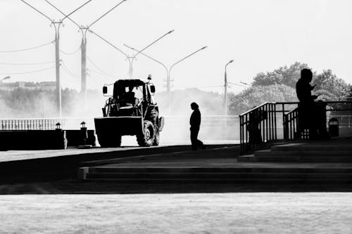 Silhouette of a Tractor Driving on a Street and People Walking on Sidewalk 