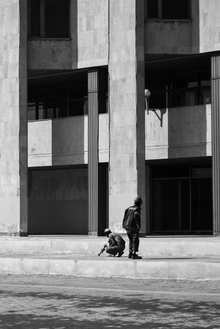 Two men working outside a building captured in artistic black and white.