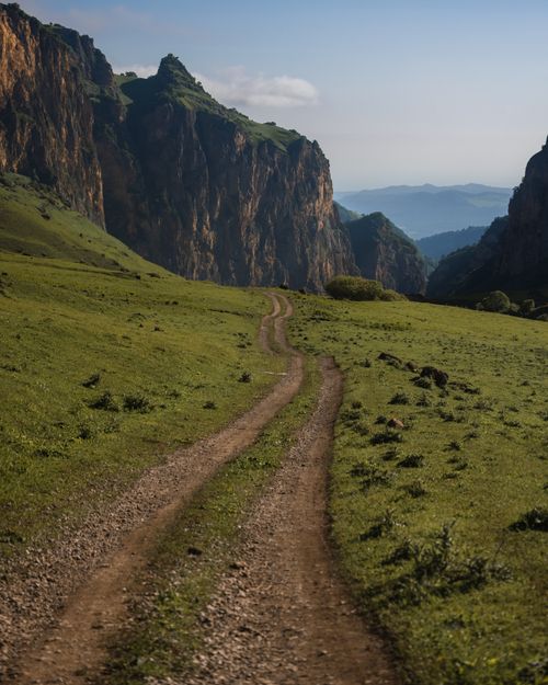 Free A serene mountain road winding through lush greenery and rugged cliffs under a clear blue sky. Stock Photo