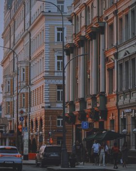 A vibrant city street showing historic European architecture with cars and pedestrians.