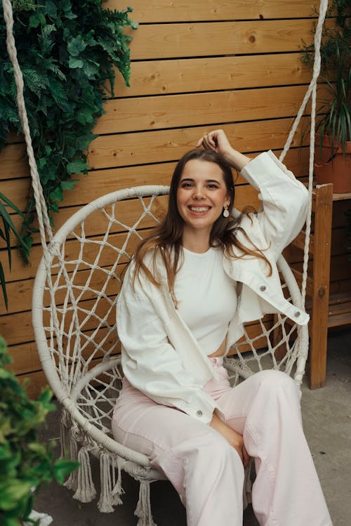 Woman in White Crop Top and Long Sleeve Jacket Sitting on a Macrame Swing