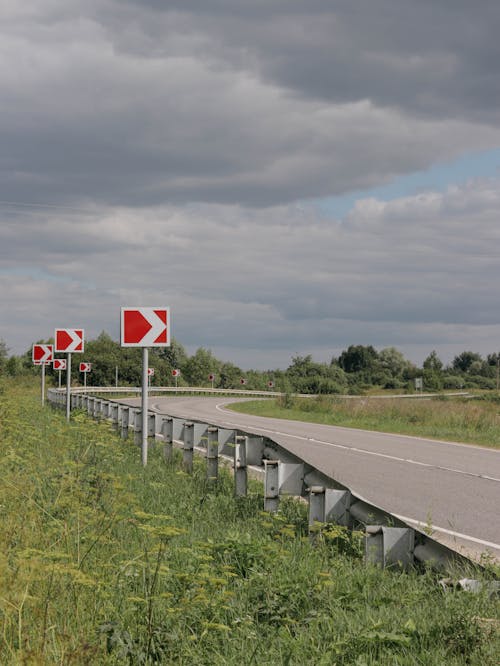 An Empty Road Near the Green Grass Under the White Clouds