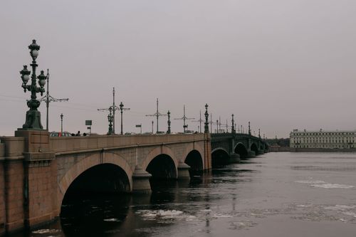 Free A picturesque stone bridge spanning a winter river with scattered ice, under an overcast sky. Stock Photo