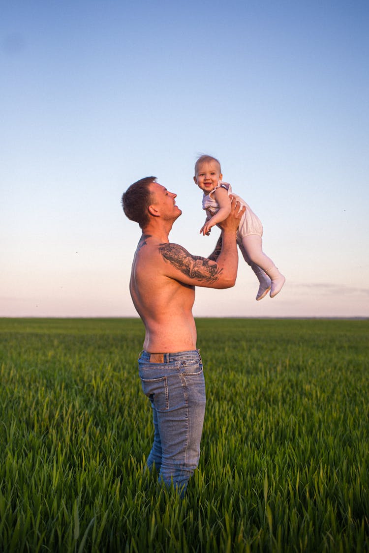 Father Holding His Little Daughter On A Field 