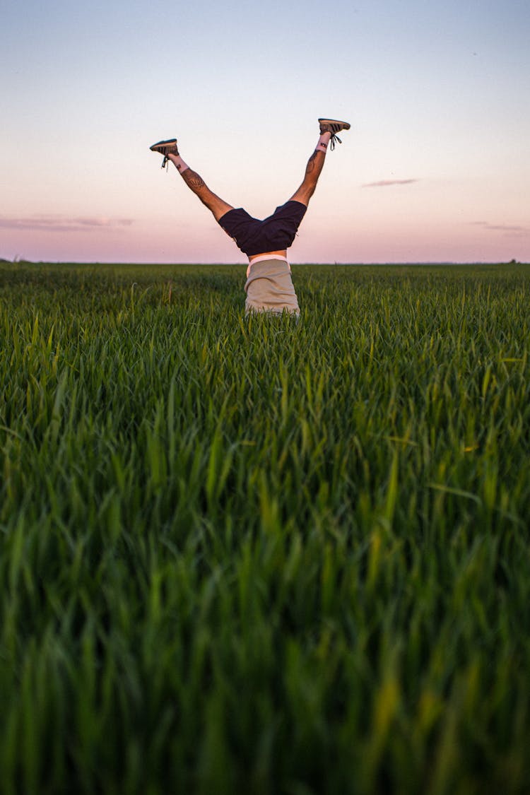 Person In Black Shorts Standing Upside Down On Green Grass Field 